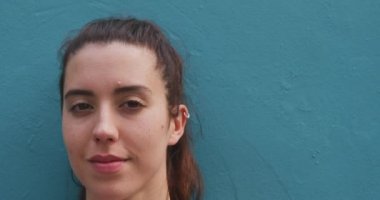 Portrait close up of a Caucasian woman on her way to fitness training, standing in the street against a blue wall, turning and looking to camera and smiling, slow motion