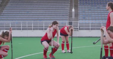 Hokey sopalarını tutan ve maçı kaybettikten sonra sahada diz çöken beyaz kadın hokey oyuncularından oluşan bir takımın yan görüntüsü. Arka planda galibiyetlerini kutlayan takım, yavaş çekim.