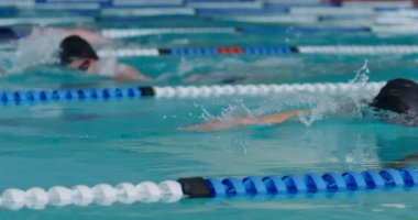 Side view of multi-ethnic group of male swimmers at swimming pool, racing each other in lanes, swimming crawl in slow motion