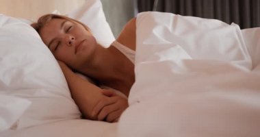 Front view of a Caucasian woman enjoying quality time in a hotel, lying on bed in bedroom, sleeping, slow motion