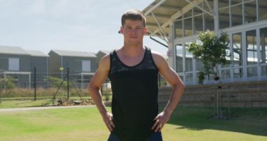Portrait of a Caucasian male runner wearing a black vest, training at a sports field, standing with his hands on hips, looking to camera and smiling. Track and Field Sports Training in Stadium, in slow motion