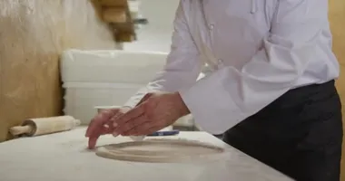Meşgul bir pizza restoranında çalışan, yemek yapmadan önce pizza hamuru hazırlayan beyaz bir aşçının portresi. Ticari mutfakta çalışmakla meşgul şefler..
