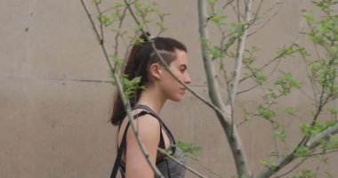 Side view of a Caucasian woman on her way to fitness training, walking in the street on a cloudy day, carrying sports bag, slow motion