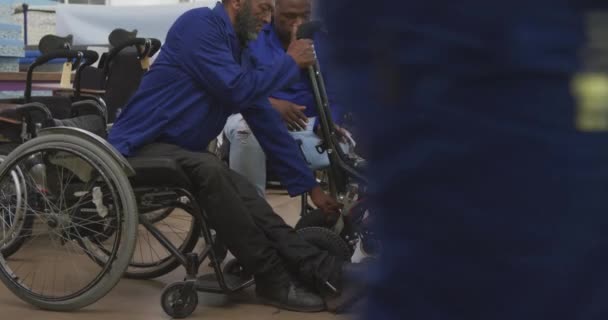 在一家制造轮椅 检查产品 主管跪在剪贴板上 在剪贴板上书写的工厂里 一组非裔美国男性工人和一名白人男性主管的侧视图 — 图库视频影像