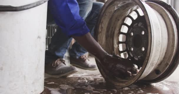 Vue de face d'un batteur de panneau mâle africain senior dans un atelier de canton, nettoyant une roue en alliage. Tourné à Capetown en Afrique du Sud .