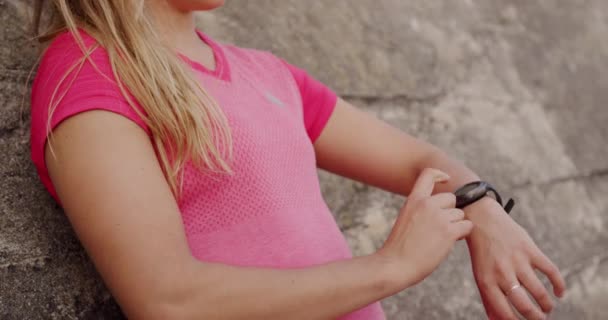 一名白种人年轻女子身穿紧靠着混凝土墙的运动服 在街上锻炼时看着手表 动作缓慢 侧面看了看中间部分 — 图库视频影像