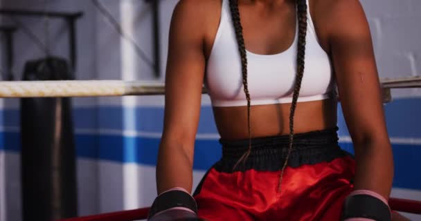 一个身披长发的混合型女拳击手坐在拳击台角落 头戴面罩 把手套撞在一起 看着镜头 准备打拳 动作缓慢 — 图库视频影像