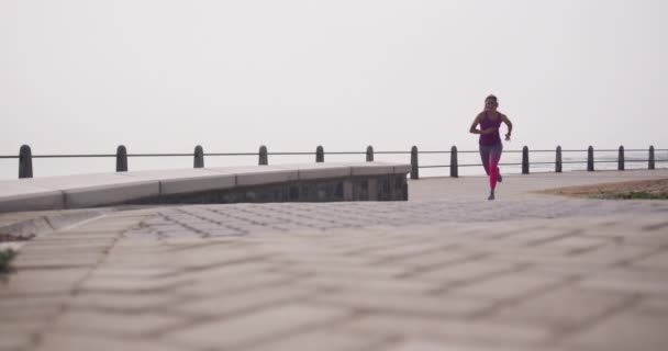 遊歩道でのワークアウト中に走るスポーツウェアやヘッドフォンを身に着けている若い白人女性のフロントビュー スローモーション — ストック動画