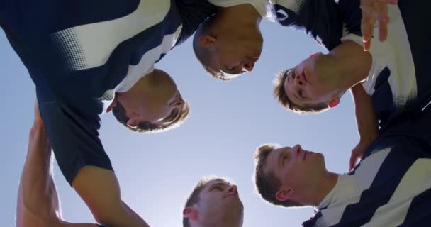 低视角 抬头看着一群多种族的男子橄榄球选手 他们在一个充满激情的拥抱中在球场上训练 讨论着比赛计划 手挽着肩膀 动作缓慢 — 图库视频影像