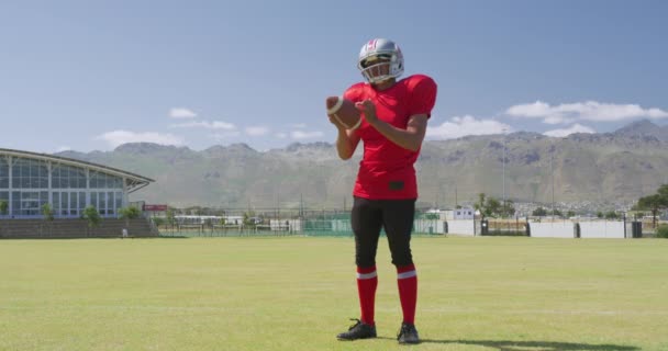 アメリカンフットボール選手がボールを保持し ゆっくりとした動きで スポーツフィールドで彼の手でそれと遊ぶのサイドビュー 陸上競技場での陸上競技トレーニング — ストック動画