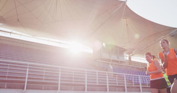 10代の白人女性ホッケー選手のチームのサイドビュー 太陽の下でスタジアムでピッチの周りを実行 ホッケーをプレイする前に温暖化 レンズフレア スローモーション — ストック動画