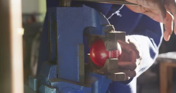 一个非裔美国人在一家制造板球球的工厂的车间里工作 站在工作台上收紧板球球的恶习 慢动作 他的镜头正中 — 图库视频影像