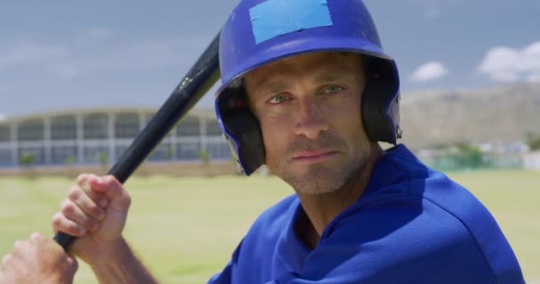 野球チームのユニフォームを着てヘルメットをかぶってスポーツフィールドでトレーニング野球バットを保持しスローモーションでピッチでスイングする準備ができて — ストック動画