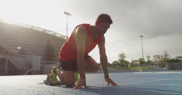 スポーツ競技場で練習している白人男性アスリートの側面図は 実行ブロック スローモーションから春を開始します 陸上競技場での陸上競技トレーニング — ストック動画