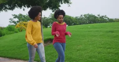 Side view of two mixed race women enjoying free time in a park side by side, walking and talking, in slow motion