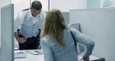 Front view of a mixed race man in suit working in an office, greeting a Caucasian blond woman and making notes
