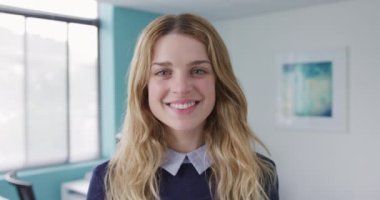 Portrait of a happy Caucasian woman with long blond hair working in a creative office and looking at camera smiling