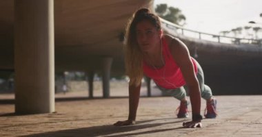 Front view close up of a young Caucasian woman wearing sports clothes doing push-ups during a workout in the morning, slow motion.