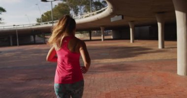 Sabahleyin köprünün altında spor giysiler içinde koşan beyaz bir kadının arkadan görünüşü, yavaş çekim.