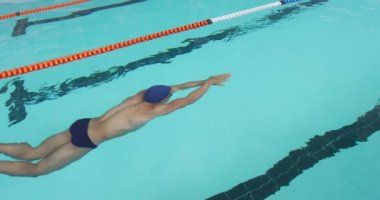 Side view of Caucasian male swimmer at swimming pool, swimming under water in a lane during a competition, doing the crawl stroke, in slow motion