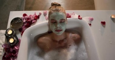 Front view of a beautiful Caucasian woman enjoying quality time in a hotel bathroom, lying in bathtub, in slow motion