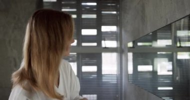 Side view of a beautiful Caucasian woman enjoying quality time in a hotel bathroom, brushing hair in bathroom, slow motion