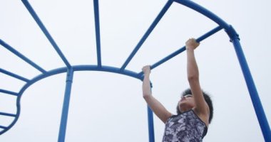 Çocuk parkında boş vakit geçiren, barfiks çeken melez bir kadının düşük açılı ön görüntüsü.