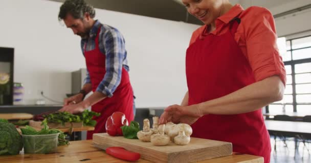 在烹饪课上 一位高年级的白人男女正在做饭 在木制切菜板上切蔬菜 站在餐馆餐桌旁 慢吞吞地站着 侧视图 — 图库视频影像