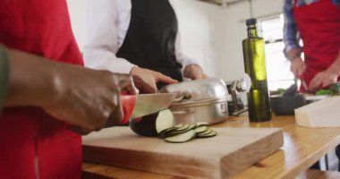 Kafkasyalı bir adam ve Afrikalı bir kadının yemek pişirme kursunda yemek hazırlarken yan görüntüsü. Beyazlı beyaz kadın şef öğrencilerinin yavaş çekimde birlikte çalışmalarını izliyor.