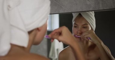 Over the shoulder view of a Caucasian woman enjoying quality time in a hotel, brushing teeth in bathroom, reflected in mirror, slow motion