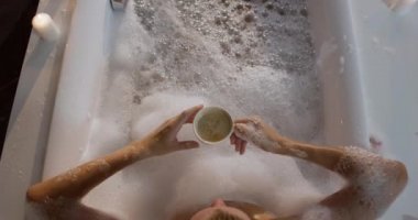 Beyaz bir kadının yüksek açılı ön görüntüsü, otelde kaliteli zaman geçirmesi, küvette uzanması, kahve içmesi, yavaş çekim...