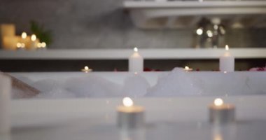 Side view close up of a Caucasian woman enjoying quality time in a hotel, lying in bathtub with candles, slow motion