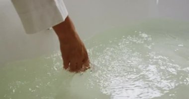 Close up of a hand of a Caucasian woman enjoying quality time in a hotel, playing with water in a bathtub, checking temperature, slow motion