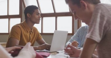 Sınıfta oturan, birlikte çalışan, dizüstü bilgisayar kullanan, konuşan ve gülümseyen çok ırklı genç erkek ve kadın okul öğrencilerinin yan görüntüsü.