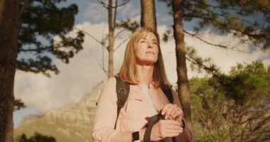 Kafkasyalı üst düzey bir kadının doğanın tadını çıkarırken İskandinav yürüyüş sopalarıyla ormanda durup ağır çekimde gülümserken görüntüsü.