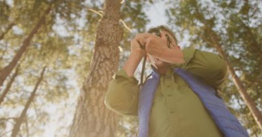 Yaşlı beyaz bir adamın doğada vakit geçirmesinin ön görüntüsü, yürüyüş sırasında ormanda duruyor, kamerasıyla yavaş çekimde fotoğraf çekiyor.