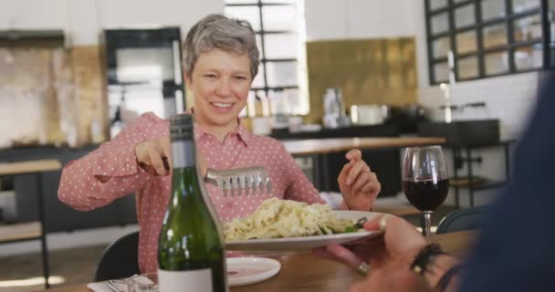 在餐馆厨房上完烹饪课后 一位白种人老年妇女坐在餐桌旁和同事们放松一下 慢吞吞地谈着话 端着刚烹调好的面食 — 图库视频影像