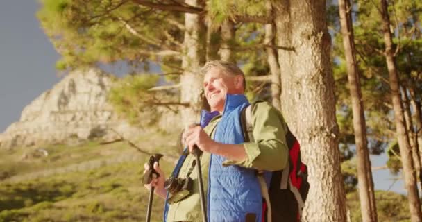 ノルディックウォーキングスティックとハイキング中に森の中に立って 自然の中で時間を楽しんでいる上級白人男性のフロントビューは 笑顔とスローモーションで彼の手を上げる — ストック動画