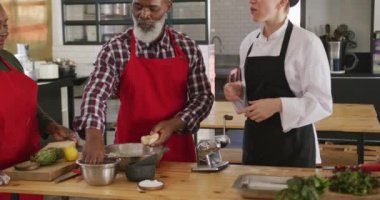 Restoran mutfağında aşçılık kursunda yemek hazırlayan ve talimatları dinleyen kıdemli Afrikalı Amerikalı bir adamın ön görüntüsü. Yavaş çekimde hamura un ekliyor.