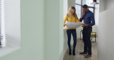 Kafkasyalı bir kadın ve melez bir adamın yaratıcı bir ofiste çalışıp mimari planlara bakıp koridorda el sıkıştığına dair ön görüş.