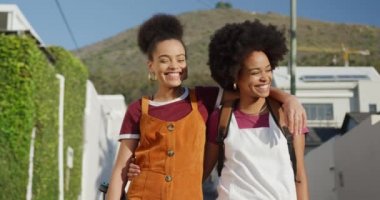 Güneşli bir günde sokakta boş vakit geçiren, yürüyen, kucaklayan, ağır çekim iki melez kadının ön görüntüsü.