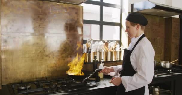 Boční pohled na kavkazskou kuchařku na kuchařské hodině v kuchyni restaurace, která smaží čerstvou zeleninu ve vyhřívaném woku a ve zpomaleném filmu je zapálí.