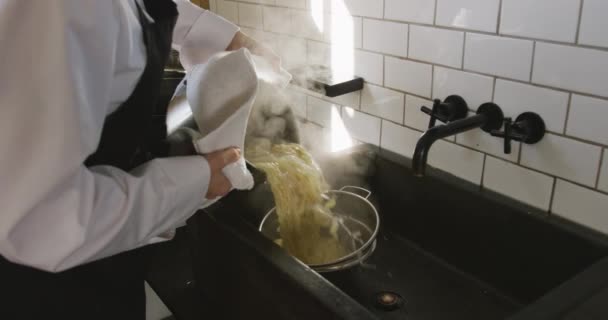 レストランのキッチンで調理教室中に白人女性シェフのサイドビューの真ん中のセクション シンクのザルに鍋から新鮮な調理パスタを排出 スローモーションで — ストック動画