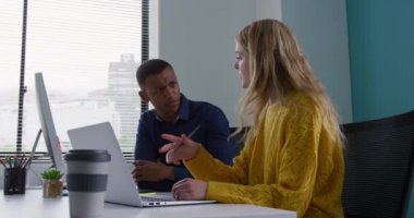 Kafkasyalı bir kadın ve yaratıcı bir ofiste çalışan, bilgisayar ekranına bakan, tartışan, ağır çekimde çalışan melez bir adamın yan görüntüsü.