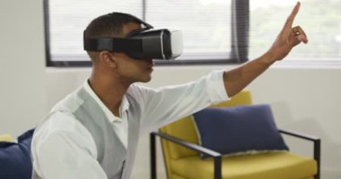 Yaratıcı bir ofiste çalışan, VR kulaklık takan, etrafa bakınan ve sanal interaktif ekrana dokunan melez bir adamın ön görüntüsü.