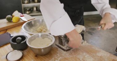 Restoran mutfağında aşçılık kursunda, makarna makinesinde hamuru ağır çekimde yuvarlayan beyaz bir kadın şefin yan görüntüsü.