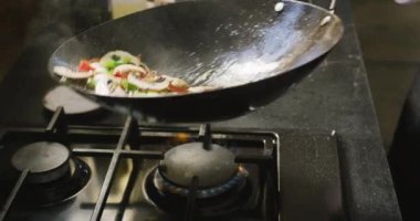 Restoran mutfağındaki aşçılık sınıfındaki beyaz bir kadın şefin elini yüksek açılı olarak yakın plan çek, tavayı tut, taze sebzeleri kızart ve yavaş çekimde fırlat.