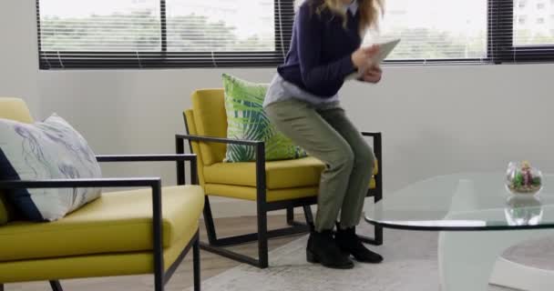 Vue latérale d'une femme caucasienne travaillant dans un bureau créatif, assise dans un fauteuil dans un hall, à l'aide d'une tablette 