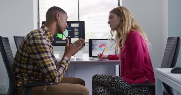 創造的なオフィスで働く白人女性と混合人種の男の側面図 コンピュータとラップトップのコンピュータ画面を見て 議論し 女性はノートを作る スローモーション — ストック動画