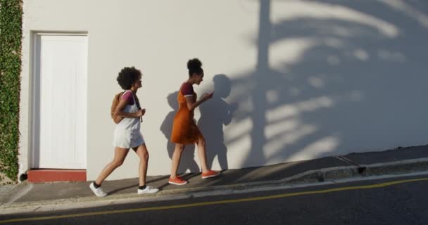 两个混血儿在街上享受着自由时间 在阳光灿烂的日子里一起散步和使用智能手机 慢动作的侧视图 — 图库视频影像